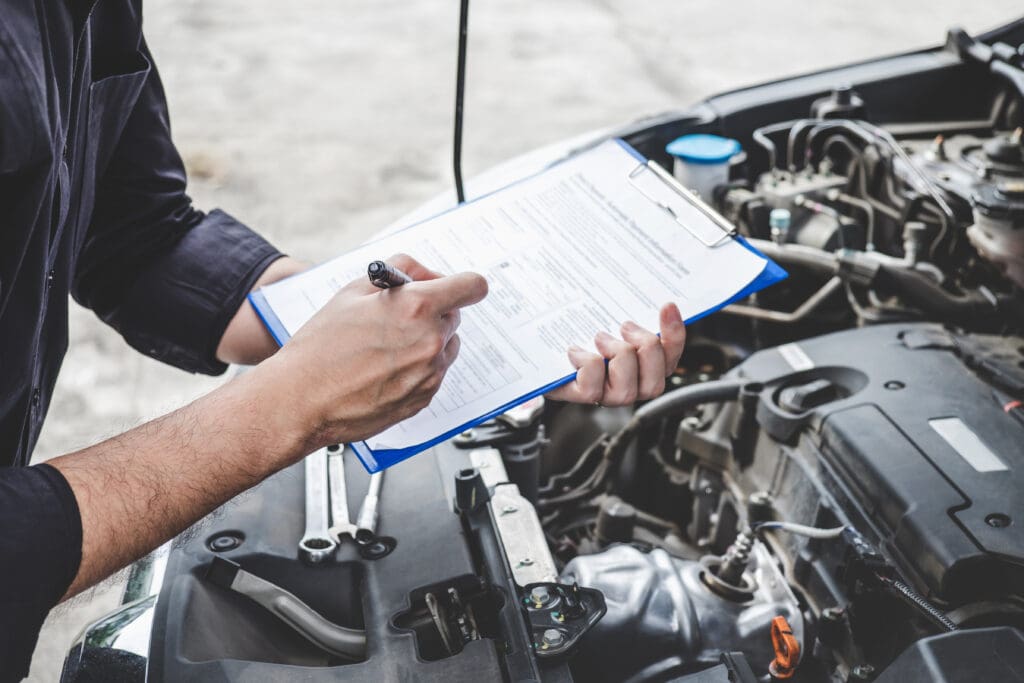 A person in a dark shirt holds a pen and clipboard, meticulously inspecting a car engine bay during vehicle maintenance. The hood is open, exposing the engine components. Notes are taken on necessary car servicing like DPF cleaning to ensure optimal performance.