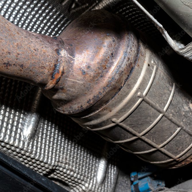 Close-up view of a rusted catalytic converter beneath a vehicle, highlighting the textured metal surface and cylindrical shape with a welded pipe—a crucial component often inspected during comprehensive car servicing.